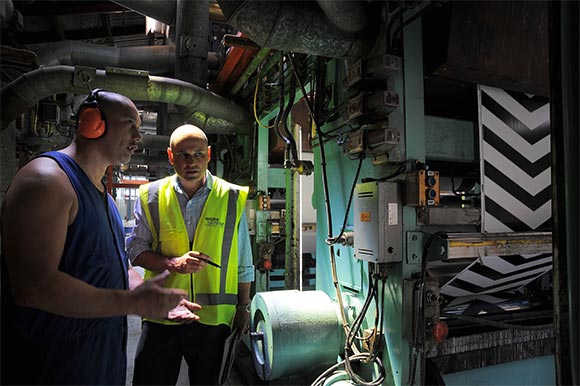 [Image] Manufacturing workers inspecting a printing machine, working in a confined space. 