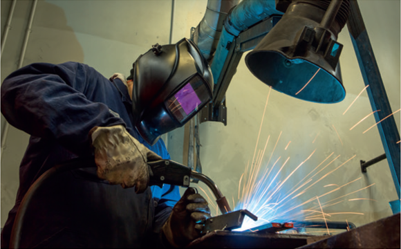 [image] Man at workstation wearing protective clothing and helmet